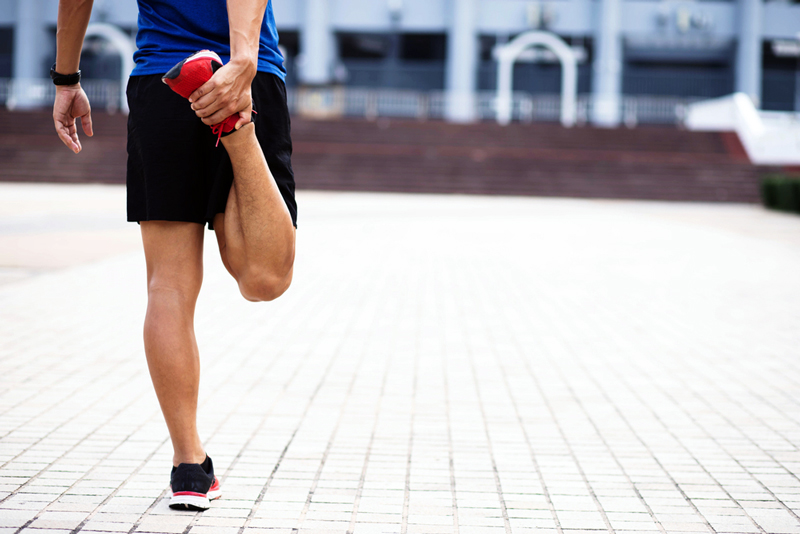 A male runner stretching his leg by bending his knee behind him